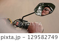 POV of motorcycle passenger with driver reflection in rearview mirror on a rural road. Over the shoulder shot of man riding motorbike on road. Handlebar, throttle handle and speedometer of scooter. 129582749