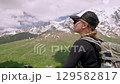 Woman hiker admires view of Svaneti mountains in Greater Caucasus. Female with backpack outdoors hiking. Mountain trekking adventure. Nature travel experience. Green hills, snow-capped peaks. Slowmo 129582817