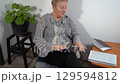 An elderly woman is sitting in a chair and reading a textbook. A grandmother takes a textbook and reads 129594812