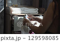 Sunlight illuminates a pregnant woman as she carefully folds tiny white baby clothes in a dresser drawer in preparation for the arrival of her baby. Pregnant woman sorts through baby clothes. 129598085