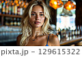 A blonde woman is smiling and enjoying her time in a vibrant bar filled with glowing lights. The atmosphere is inviting as she speaks with friends, showcasing her stylish look. 129615322