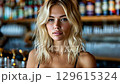 Blonde woman with wavy hair is seen in a cozy bar ambiance. 129615324
