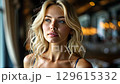 A blonde woman captures attention with her elegant presence in a chic cafe. The warm lighting enhances her features as she enjoys a moment of serenity. 129615332