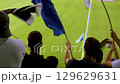 View from behind of fans with flags against the backdrop of a football field. 129629631