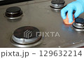 Female hands in blue gloves cleaning kitchen stove. Cleaning with orange cloth in kitchen settings. House hygiene. 129632214
