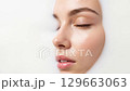 A detailed close-up of a youthful person's face with clear, hydrated skin, partially submerged in a milky white bath, emphasizing purity, wellness, and natural beauty. 129663063