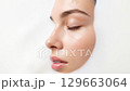 A serene close-up shot captures the side profile of a young female face with water droplets, resting peacefully in a white, milky bath, emphasizing beauty and wellness. 129663064