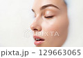 A beautiful young woman's face, with closed eyes and a tranquil expression, is immersed in a white liquid, highlighting concepts of purity, relaxation, and dermatological care. 129663065
