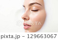A beautiful close-up of a young woman's serene face with closed eyes, gently bathed in white liquid, symbolizing purity, skincare, and tranquility. 129663067