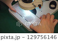 Quality control of LED panel production. Close-up of hand of technologist checking LED panel through microscope. Researcher holds LED panel in hand, looks through microscope. High-precision equipment 129756146