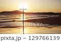 Waves rolling into a sandy beach reflecting a red sunset and strong light, with the Holy Cross of Jesus Christ in the background. 129766139