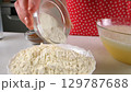 Baker woman adding baking powder to flour in white bowl cooking on kitchen. 129787688