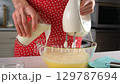 Pastry chef woman hands adding milk to batter while whisking with electric mixer 129787694