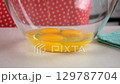 Eggs falling into glass bowl on white table on kitchen at home. 129787704