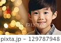 Smiling boy in a white shirt posing in front of a lit Christmas tree with colorful glowing lights. Asian boy. zoom in, zoom out, pan, or 360 degree shot, animate 129787948