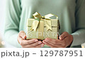 Close-up of hands holding a sparkling green gift box with a bow, set against a soft green festive background. zoom in, zoom out, pan, or 360 degree shot, animate 129787951