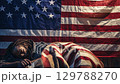 Man sleeping under a blanket with the American flag as a backdrop, highlighting themes of homelessness and patriotism. zoom in, zoom out, pan, or 360 degree shot, animate 129788270