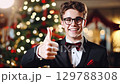 Smiling young man in a suit and bow tie posing in front of a festive Christmas tree with glowing lights. zoom in, zoom out, pan, or 360 degree shot, animate 129788308