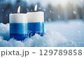 Peaceful winter candle scene with falling snow in tranquil outdoor setting. Independence day of Finland. Blue and white burning candles.Merry Christmas. Happy New Year 129789858