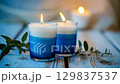 Scented candles flickering on rustic table with soft leaves and warm glow. Idependence Day of Finland. Blue and white burning candles. Happy New Year. Merry Christmas 129837537