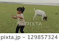 slow motion of toddler girl running with goat on grass field near the river 129857324
