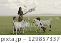mother with toddler girl feeding a tree branch to the goat on grass field near the river 129857337