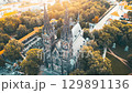 Witness the breathtaking sunrise illuminating Vysehrad Basilica of St. Peter and St. Paul in Prague. A serene morning view captured from above showcases the tower and surrounding lush greenery. 129891136