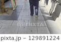 Visually impaired person walking down the street with a white cane. Casual urban walkway perspective: sidewalk movement and shadows of pedestrians 129891224