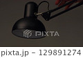 Black desk lamp with adjustable metal arm, hand turning on bright modern light 129891274