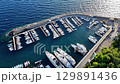 Vibrant marina filled with luxurious yachts along a scenic coastline during bright daylight hours 129891436