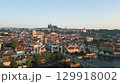 Morning light highlights the beauty of Prague as a drone soars above the Vltava River, showcasing iconic landmarks like the Charles Bridge and Prague Castle against a clear sky. 129918002