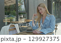 Blonde Woman Enjoying Morning Coffee Outdoors At Cafe Terrace In Blue Outfit 129927375