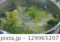 Fresh broccoli florets are submerged in boiling water, bubbling vigorously as they cook. 129965207