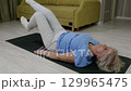 Elderly woman performing leg raises and bridge exercises on a mat 129965475