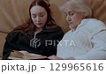 Granddaughter reading a book to her grandmother 129965616