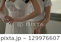 Bride adjusting wedding ring while bridesmaid fixing dress. 129976607
