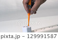 Test Plug Current with Hand Holding Orange Insulated Screwdriver Tool for Electrical Safety, Power Plug Adapter, White Extension Socket, Indoor Maintenance, Caution for Electricity Testing 129991587