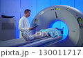 Medical worker standing confidently near MRI tunnel while female patient resting on table. Overseeing post-scan procedure inside professional medical imaging center. Patient lying on CT, PET, or MRI 130011717