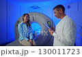 Handsome Caucasian Doctor talking to patient before MRI. Patient talking about symptoms before tomography. Patient sitting at CT scanner doctor adjusting MRI capsule. Conducting advanced imaging 130011723