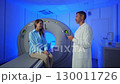 Handsome Caucasian Doctor talking to patient before MRI. Patient talking about symptoms before tomography. Patient sitting at CT scanner doctor adjusting MRI capsule. Conducting advanced imaging 130011726