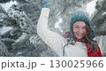 Woman Laughing and Playing in Fresh Winter Snow Next to Decorated Christmas Tree 130025966