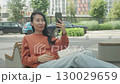 Joyful Woman Laughing During Video Call While Sitting On City Bench 130029659
