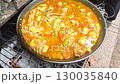 Stirring and flavoring rich seafood paella in large pan outdoor cooking scene 130035840