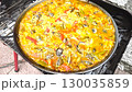 Sizzling seafood paella cooking over open flame in vibrant outdoor setting 130035859