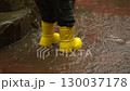 child in yellow raincoat and yellow boots jumps in puddles under the rain in slow motion 130037178