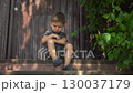 Child is angry and crosses arms showing frustration on a porch during a hot summer day in dark clothes 130037179