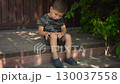 the boy sits on the porch on a hot summer day gently touching a scab on his knee with his finger the camera slowly zooms in toward his face 130037558