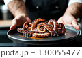 Chef is holding plate with grilled octopus, dark blurred background with copy space 130055477