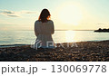 Woman wearing white dress watching golden sunset at beach 130069778