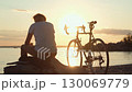 Cyclist resting at sunset on beach 130069779